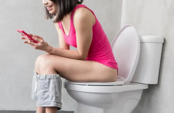Persona usando su teléfono móvil en el baño, práctica que puede causar hemorroides e infecciones según estudio científico.