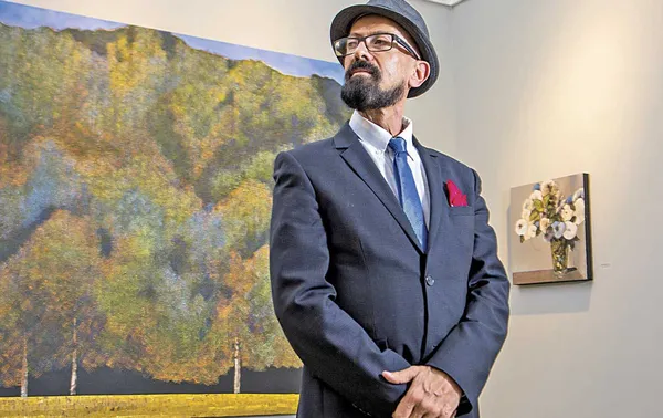 Oscar Román en su galería, de pie frente a una obra, rodeado de pinturas contemporáneas.